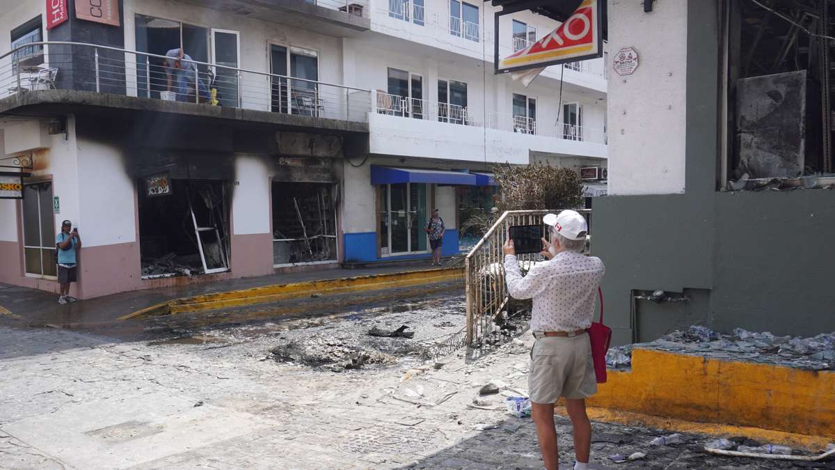 Turistas toman fotografías de comercios calcinados en Puerto Vallarta por la violencia tras la muerte en un operativo de ‘El Mencho’. Foto: EFE/Arturo Montero